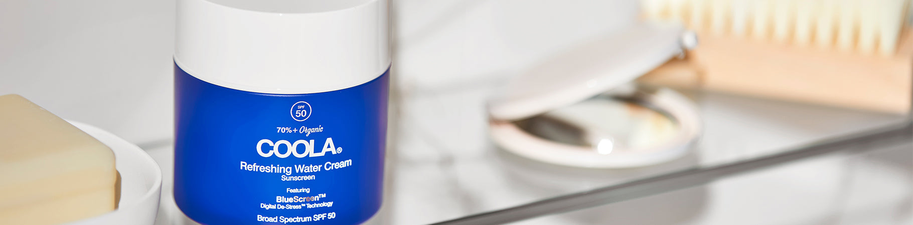 COOLA Refreshing Water Cream Sunscreen SPF 50 on a bathroom shelf beside a soap bar and mirror.