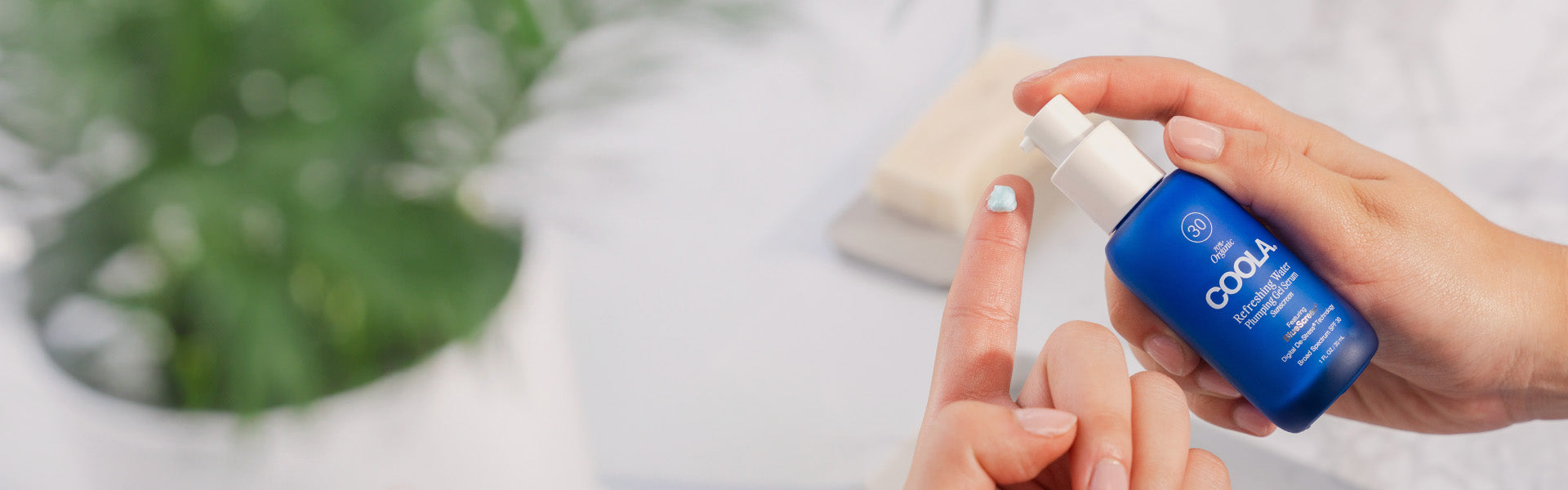 Person applying COOLA Refreshing Water Plumping Gel Cream SPF 30 from a blue pump bottle.